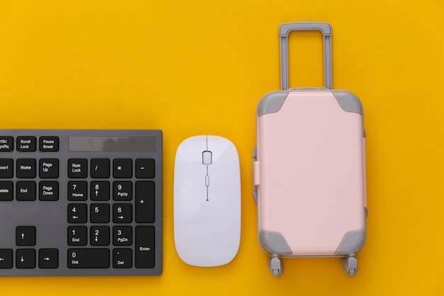 Travel concept. pc keyboard and mini travel luggages on yellow