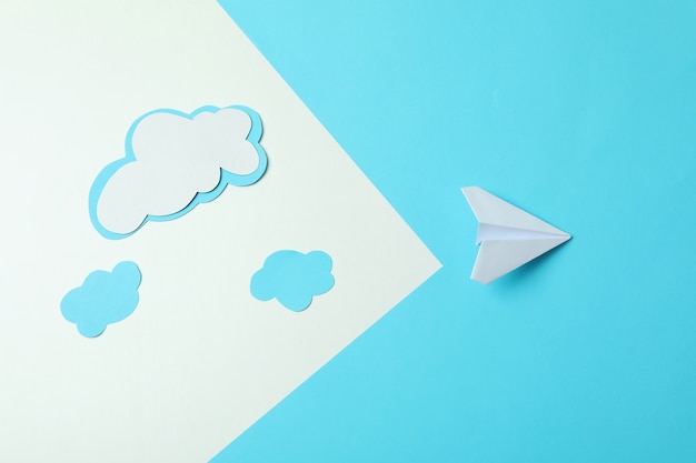 Travel concept with paper plane and clouds on two tone background