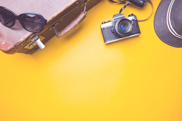 Travel concept with retro camera films suitcase sunglasses and hat on yellow
