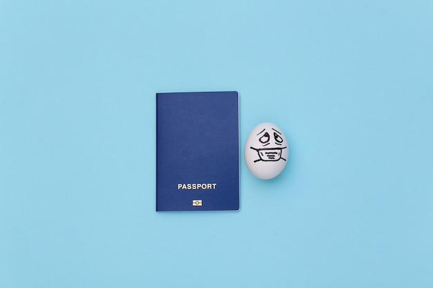 COVID-19 기간 동안 여행하십시오. 파란색 배경에 의료 마스크에 여권과 달걀 얼굴.