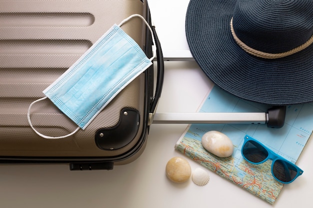 Photo travel during the time of covid-19. medical mask, suitcase, sun glasses, map, seashells on the white background. vacation, holidays in corona times. colorful design.