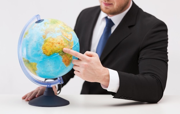 travel, earth, geography and business concept - close up of businessman pointing finger to earth globe