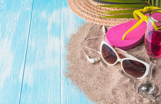 Travel equipment, eyeglasses with sandals and sun hat on blue wooden background.