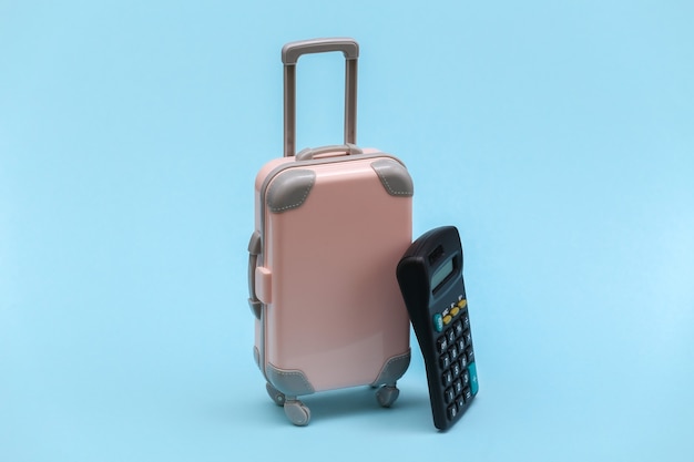 Travel expenses. Mini plastic travel suitcase with calculator on blue background. Minimal style