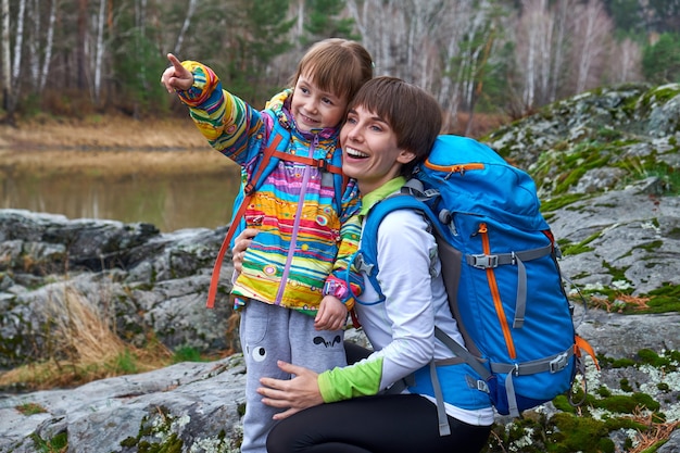 Travel family - mother and child with backpacks laugh and point with their finger to distance