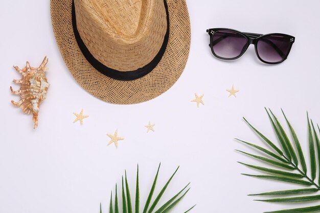 Travel flat lay Hat with sungglasses starfish seashells and palm leaves on white background Top view