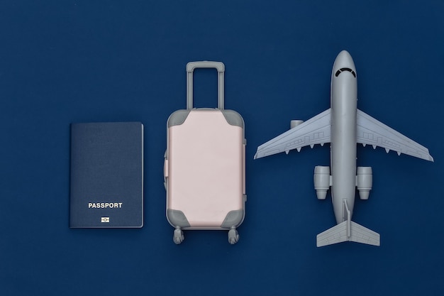 Travel flat lay. Mini plastic travel suitcase, passport, air plane on classic blue background. Minimal style. Top view