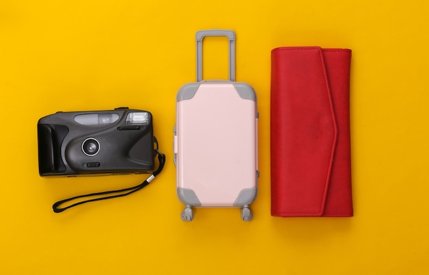 사진 여행 평면 누워. 노란색 배경에 미니 플라스틱 여행 가방, 빨간색 지갑, 카메라. 최소한의 스타일. 평면도