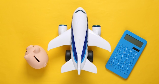 Viaggio piatto calcolatore aereo passeggeri giocattolo e salvadanaio su sfondo giallo vista dall'alto