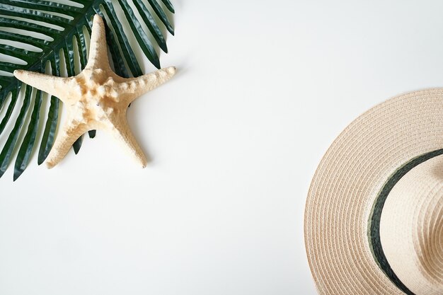 Travel flat lay. Tropical leaves and straw hat on white