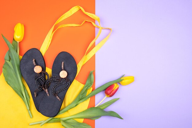 Photo travel flat lay with women sandals yellow beach bag and tulips on two color background