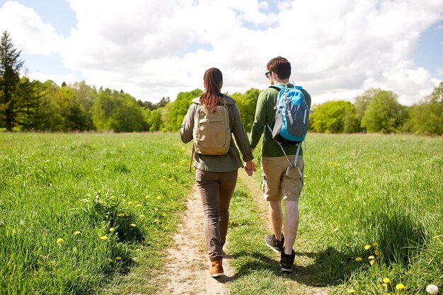 travel, hiking, backpacking, tourism and people concept - happy couple with backpacks holding hands and walking along country road