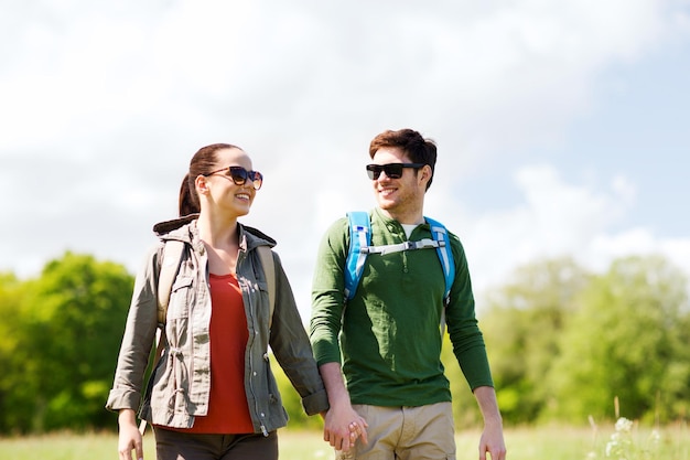 travel, hiking, backpacking, tourism and people concept - happy couple with backpacks holding hands and walking outdoors