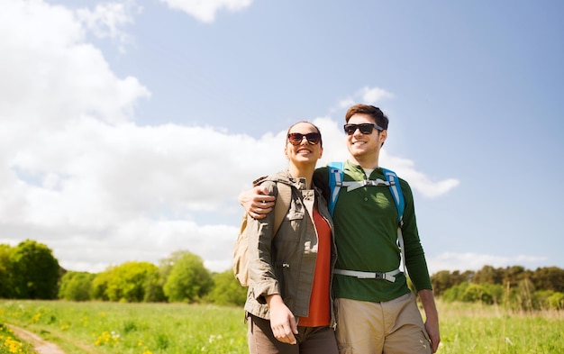 путешествия, походы, альпинизм, туризм и концепция людей - счастливая пара с рюкзаками обнимается и гуляет на свежем воздухе