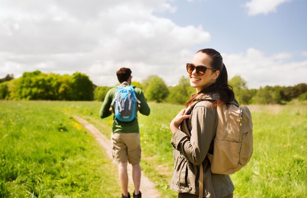 travel, hiking, backpacking, tourism and people concept - happy couple with backpacks walking along country road outdoors