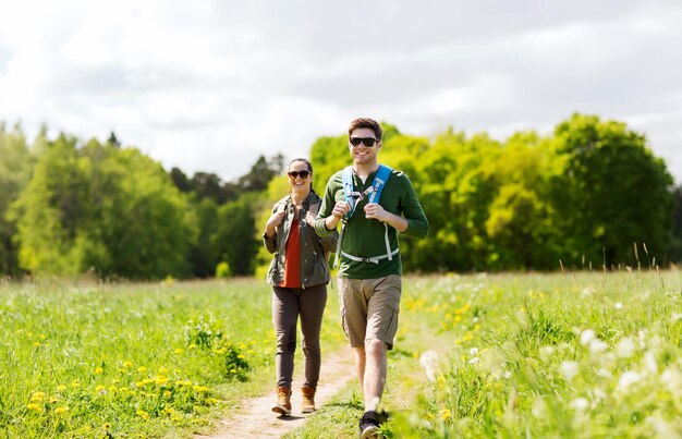 travel, hiking, backpacking, tourism and people concept - happy couple with backpacks and walking along country road outdoors