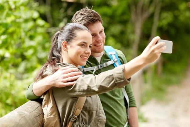 travel, hiking, backpacking, tourism and people concept - smiling couple with backpacks taking selfie by smartphone in nature