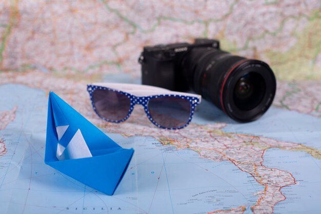 Travel holiday vacation concept origami handmade papercraft paper ship with camera and sunglasses on map near italy close up