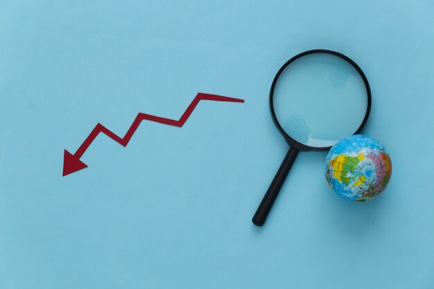 Photo travel industry decline. magnifier with globe, down arrow on a blue.