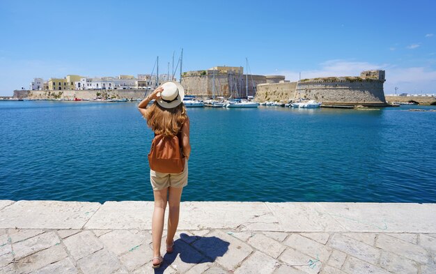 Travel in Italy. Back view of young traveler woman enjoying view of Gallipoli old town with castle, Italy, Europe.