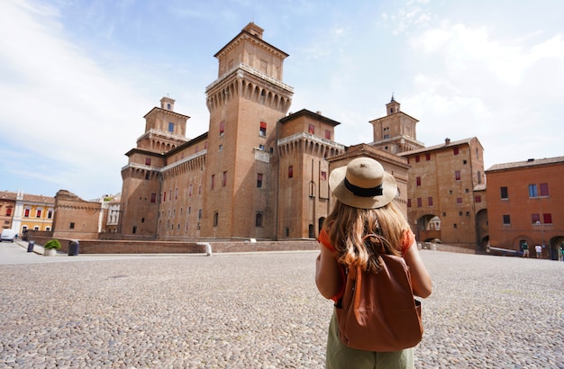 イタリア旅行。イタリア、フェラーラのエステ城（カステッロエステンセ）に向かって歩いている旅行者の女の子の背面図。