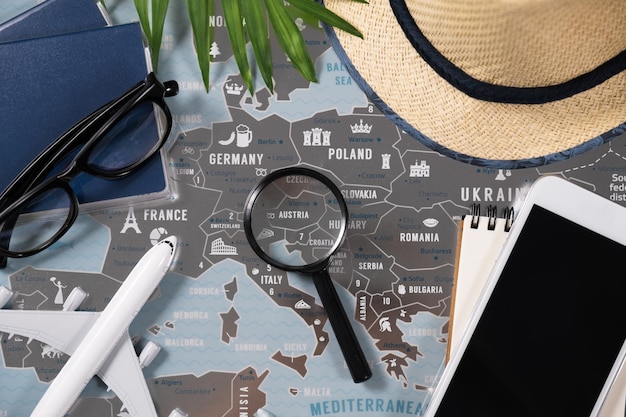 Travel items smartphone magnifying glass straw hat and\
passports on background of map of europe