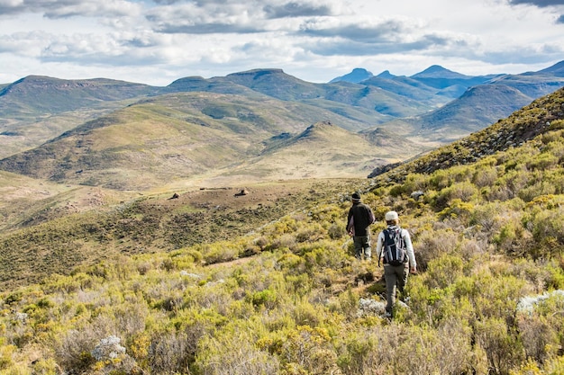 Путешествие в Лесото 2 путешественника в горах с хижинами пастухов на расстоянии
