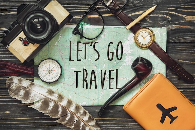 Photo travel let's go travel text sign concept on map wanderlust hipster flat lay passport compass and glasses pipe camera on black wooden background top view planning vacation explore