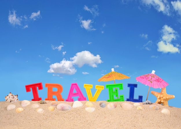 Travel letters on a beach sand against the blue sky