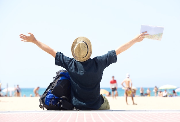 Travel man sitting by beach with arms outstretched