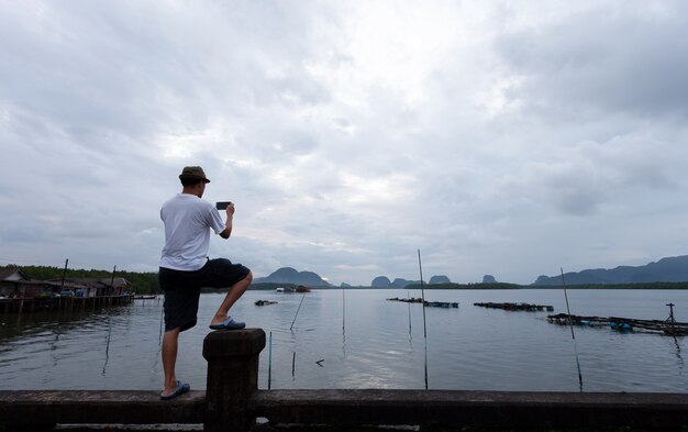 橋の上に立っている旅行者が朝日をスマートフォンで写真を撮ります。