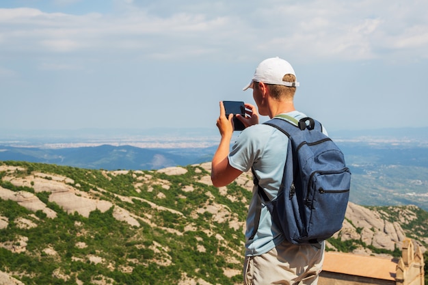 バックパック立って旅行男がスマートフォンで写真を撮るMountians晴れた日コピースペース