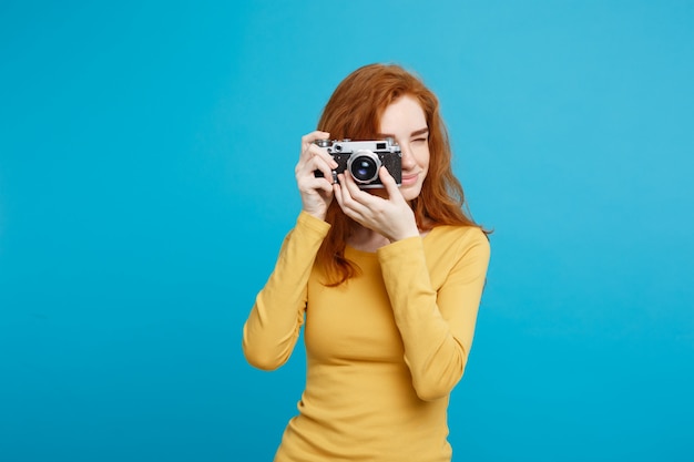 Travel and People Concept - Headshot Portrait of happy ginger red hair girl ready to travel with vintage camera in happy expression. Pastel blue background. Copy Space.