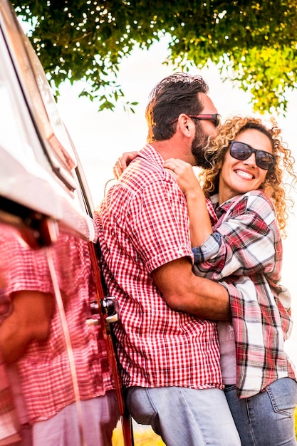 Travel people have fun hugging together outdoor with red old van vehicle adult man kissing cheerful happy middle age woman table with food and clear sky in background