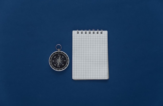 Travel planning or adventure. Compass with a notebook on classic blue background. Top view