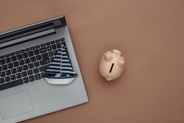 Travel Planning. Laptop and sailboat, piggy bank on a brown background. Top view. Flat lay