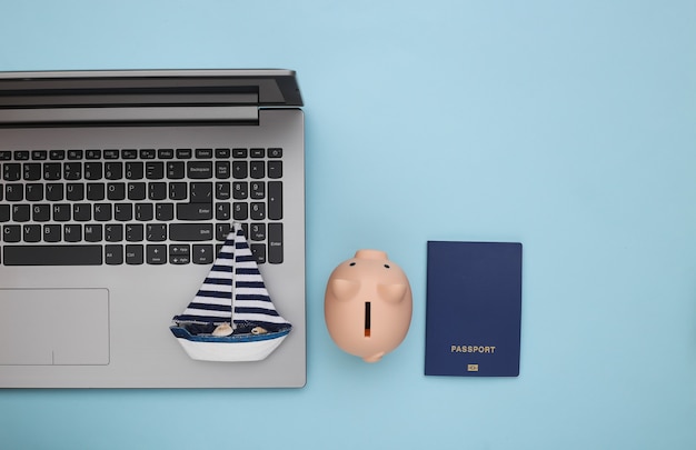 Travel Planning. Laptop and sailboat, piggy bank, passport on blue background. Top view. Flat lay