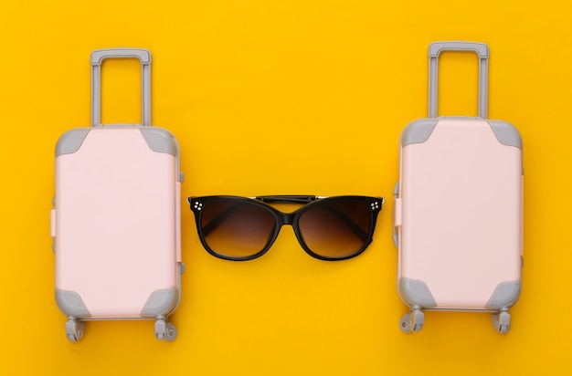 Travel planning. Two toy travel luggage and sunglasses on yellow. Flat lay