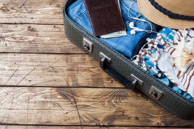 Travel preparations concept with suitcase, clothes and accessories on an old wooden table. Top view Copy space