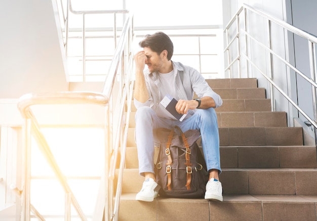 Photo travel restrictions depressed man sitting on stairs in airport flight cancelled