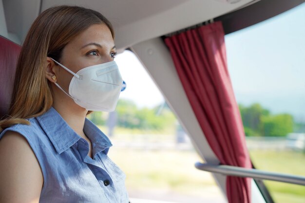 Viaggia in sicurezza sui mezzi pubblici. giovane donna con maschera protettiva kn95 ffp2 che guarda attraverso il finestrino dell'autobus durante il suo viaggio.