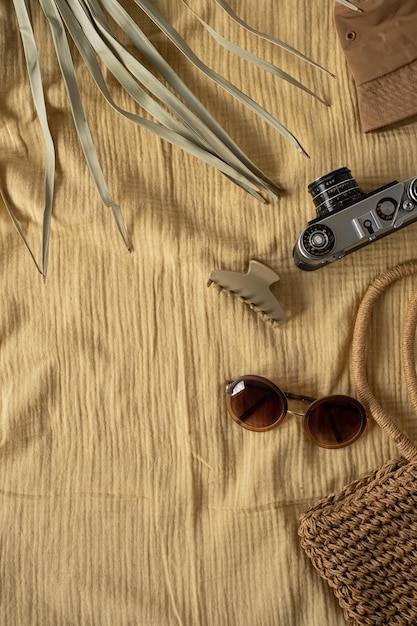Travel set panama hat hipster retro camera straw shopper bag sunglasses tropical palm leaf on yellow muslin blanket cloth Aesthetic bohemian flat lay composition for social media blog