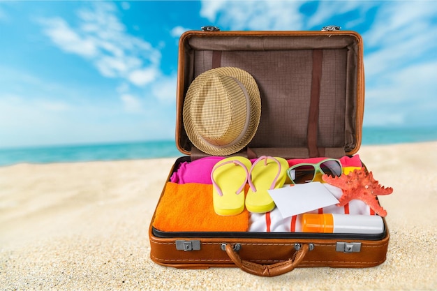 Travel suitcase with beach hat, flip-flops on beach background