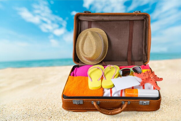 travel suitcase with beach hat, flip-flops on beach background