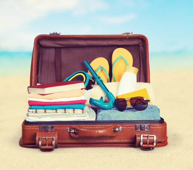 Travel suitcase with beach hat, flip-flops and retro camera on beach background