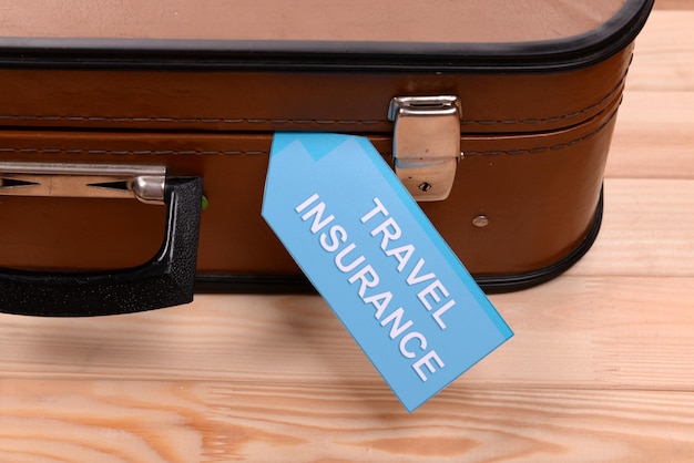 Photo travel suitcase with inscription travel insurance on wooden background