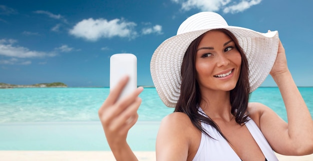 путешествия, лето, технологии и концепция людей - сексуальная молодая женщина делает селфи со смартфоном на фоне тропического пляжа