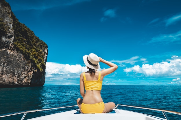 Il concetto di vacanza estiva di viaggio, la donna asiatica del viaggiatore solista felice con il bikini e il cappello si rilassa in barca sul mare a phuket tailandia