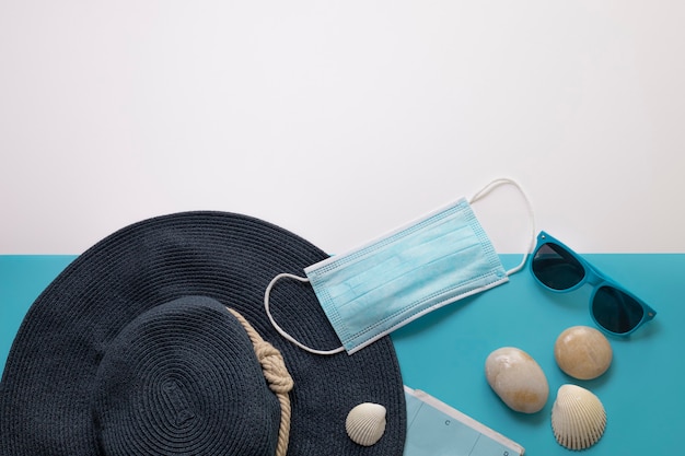 Travel during the time of COVID-19. Medical mask, sun glasses, hat, seashells on the blue and white background. Free space for text. Vacation, holidays in corona times. Colorful design.