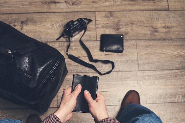 Travel and tourism and business trip concept Man sitting ready holding travel passport in hands with leather bag and photo camera on the floor